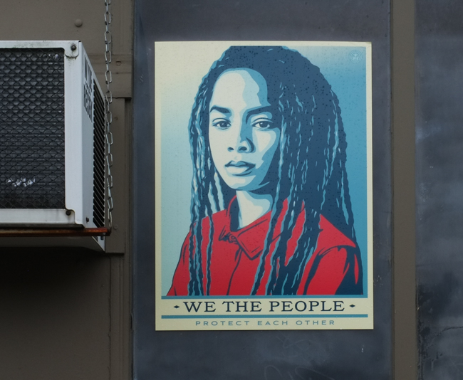 covid pandemic poster in Lynn Massachusetts, by obey aka shepherd fairey, picture of young woman, in blues and reds with text, we the people protect each other
