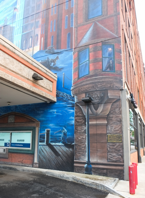 part of a mural, in blue tones, of syracuse landmarks, beside entrance to bank