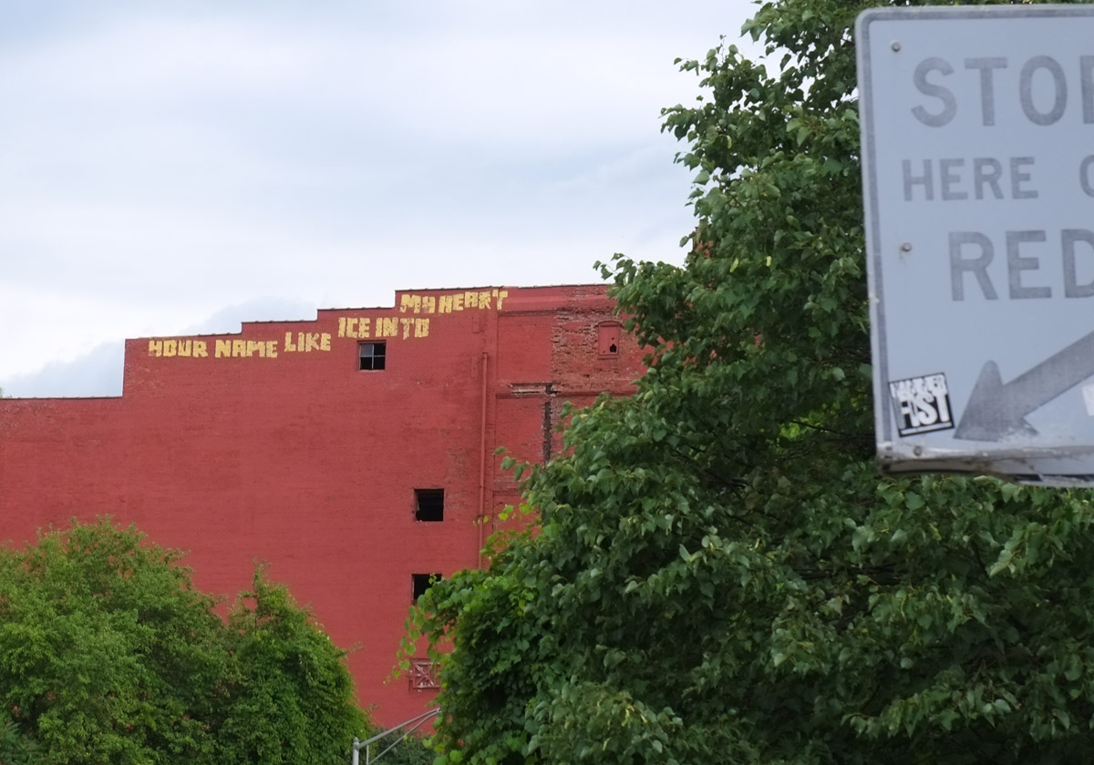 old red brick building now standing alone, with a large mural on the side of two women, one in blues and the other in reds, lots of flowers and butterflies in their hair and around them
