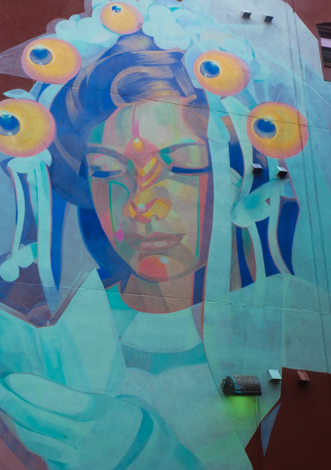 a portrait, street art mural, of a young woman at communion, religious, she is wearing a wearing veil, dress, and gloves, and she is reading in a white book, could be bible, or prayer book. 