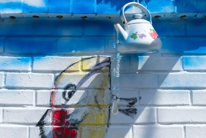 a real teapot hangs beside a painting of a fish that looks like the fish is going to kiss the teapot