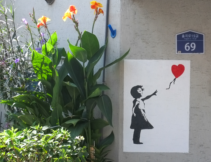 street art painting, a girl in black stencil, holds the string of a red balloon