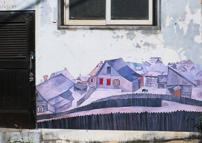 a small street art mural on the front of a house, image is a collection of houses, streets, and fences