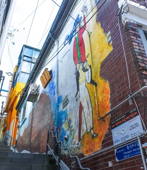 on walls, narrow street, murals, one with a man in a red jacket