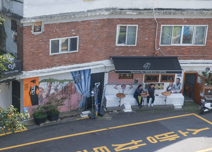 people sitting outside coffee shop, street art on walls of odeoksae coffee shop