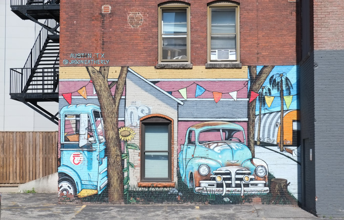 old fade blue trucks, mural by Jason Eatherly on the side of a red brick buiding with exterior metal fire escape stairs
