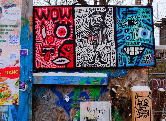 three drawings on a fence, one red, one white, one blue, lines, face, and words, he is not dead yeat, ugly, beauty