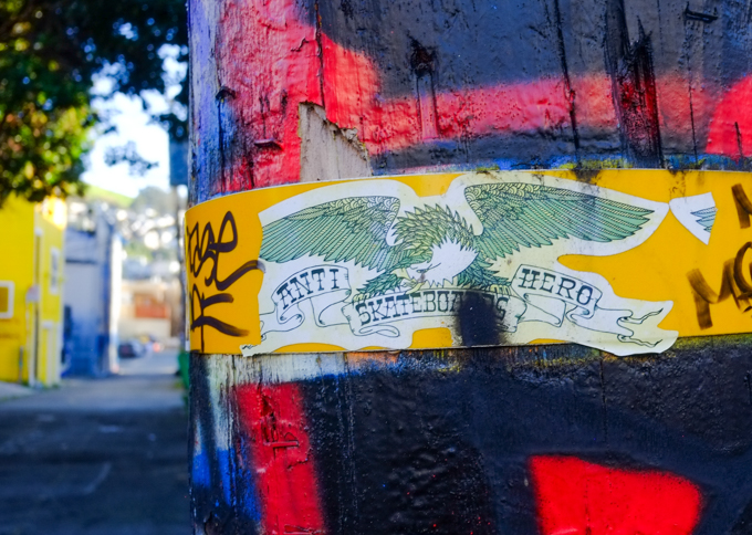 torn sticker, or paste up, on a utility pole, text says anti skateboarding hero, pole is painted black and red with graffiti