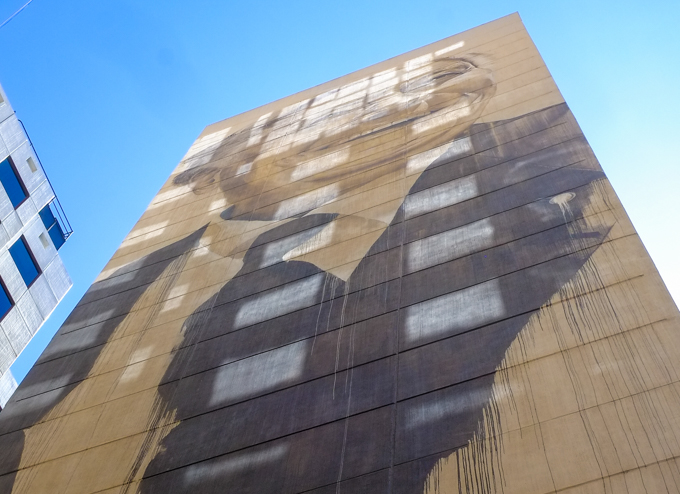 at the end of Louden Place, high up on a tall brick building, a mural by Cam Scale, a man's portrait done in black paint