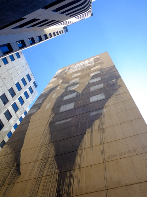 at the end of Louden Place, high up on a tall brick building, a mural by Cam Scale, a man's portrait done in black paint