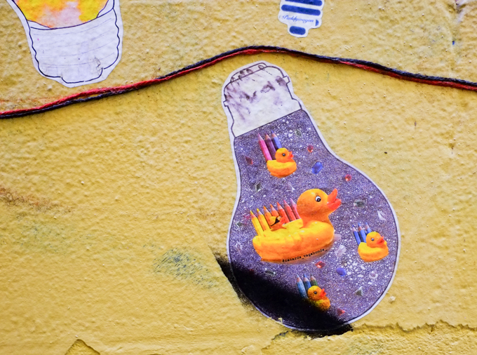 paper pasteup on yellow wall, shape of a light bulb, a group of yellow ducks, with pencil crayons, canards vagabonds