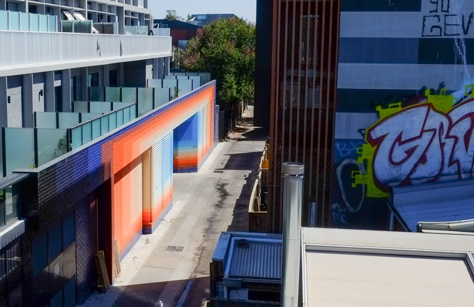 stripes forming gradients in blues and oranges along the side of a building including the door to a garage