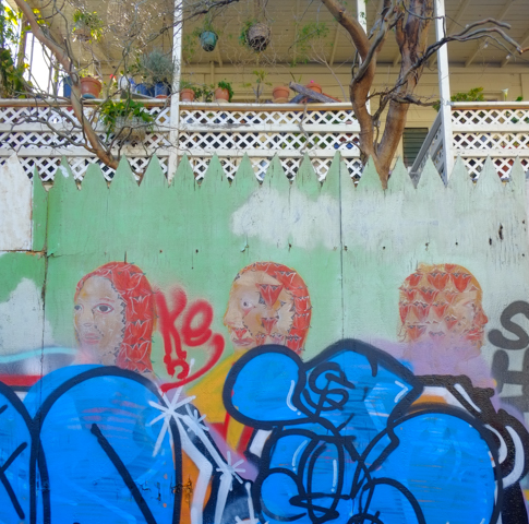 pale green mural with people that has been tagged over in blue so that just the heads of the original are visible