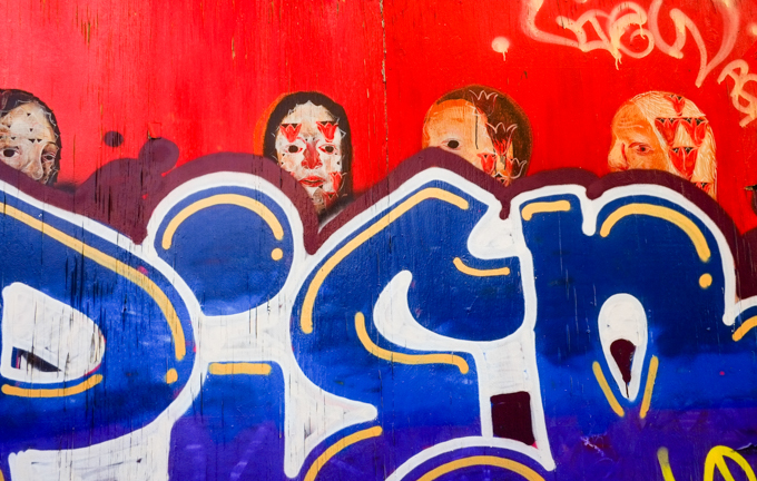 red mural with people that has been tagged over in blue and white so that just the heads of the original are visible
