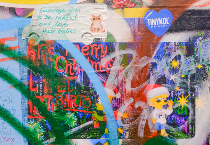 Bart Simpson spray painting Christmas messages as graffiti, Lisa Simpson in a Santa hat.