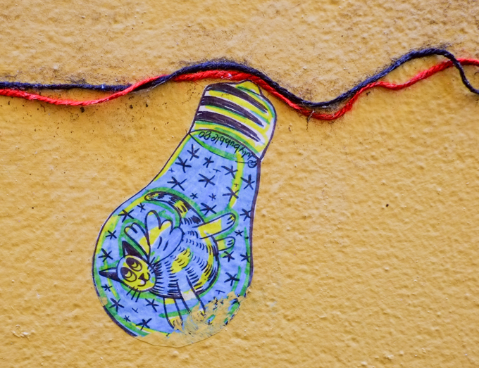 paper pasteup on yellow wall, shape of a light bulb, blue, with a cat, by julybubble80