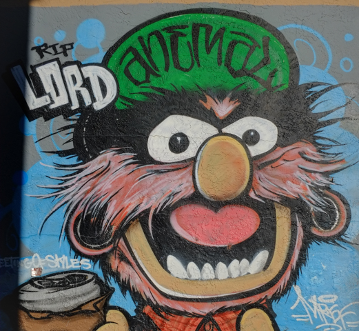 part of a street art mural, Animal from the Muppets, with a green hat that says anemal, also words on painting that say RIP Lord,