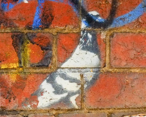 weathered black and white stencil of a pigeon, on a red brick wall