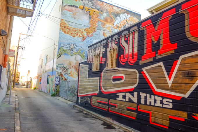 two large murals in an alley, one is text - there is so much love in this city