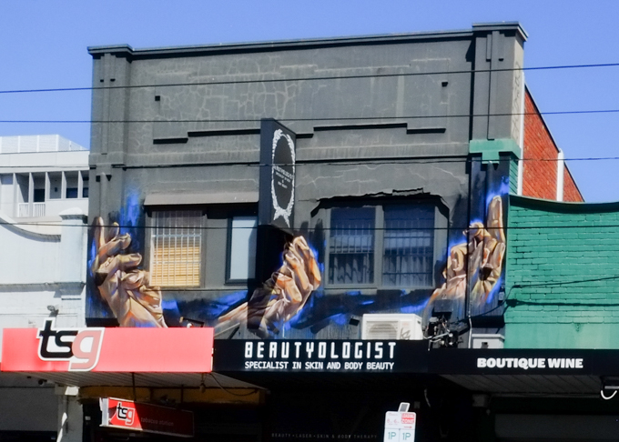 paintings of three hands on upper level of a storefront, carlisle street, melbourne