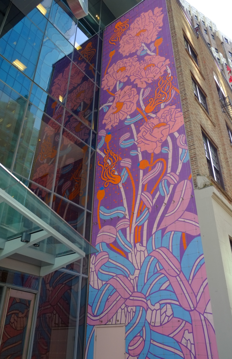 pink, purple, and blue mural of flowers, tall vertical mural beside entrance to office building, with reflections in the glass of the building