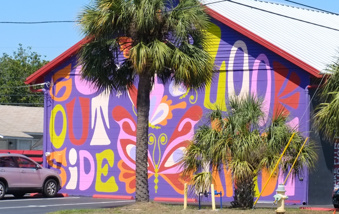 bright colour mural on the side of a building, purple background with words go outside, also butterfles