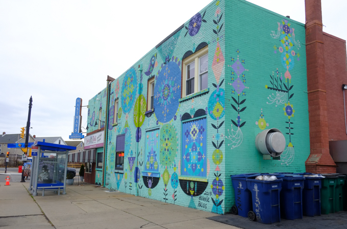 mural by Bonnie Reiss, stylized floral motifs in blues and purples on a bright turquoise background, on the side of Joe's Deli in Buffalo