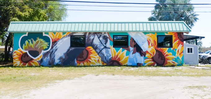 mural of a girl wearing a cowboy hat, with a horse, with many sunflowers