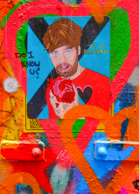 graffiti poster of a man holding an anatomically correct heart in his hand. Written over it in black marker, "Do I know you?"