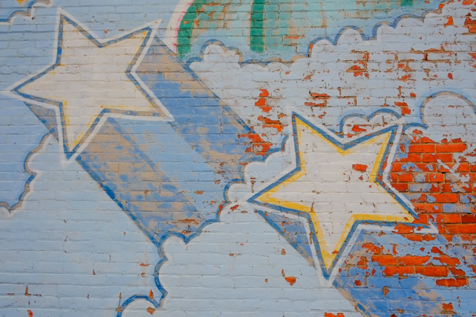 close up of shooting stars in mural, peeling paint in places, revealing red brick beneath the paint
