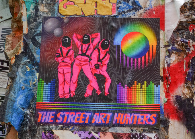 graffiti poster by the street art hunters, group of three dressed in bright pink coveralls with black masks, psychadelic colours background 