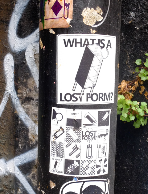 black and white stickers on a pole in an alley, both about Lost Forms,