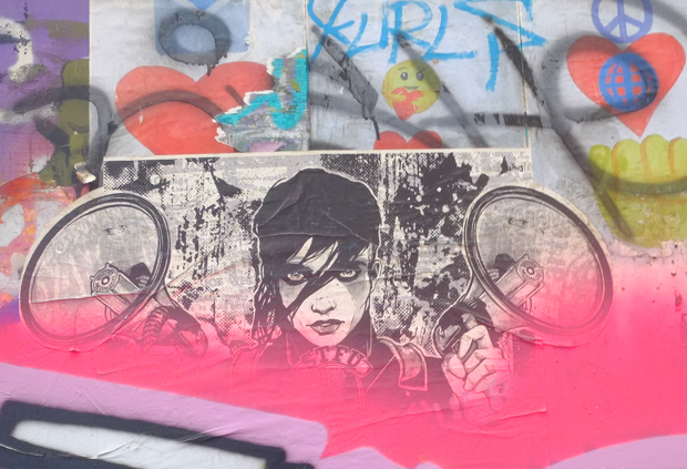 black and white paste up a woman holding up a megaphone in each hand, partially obscured with pink spray paint