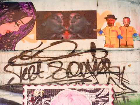 stickers and paste ups on an alley wall, above a door, one is yellow lego characters by street art hunters