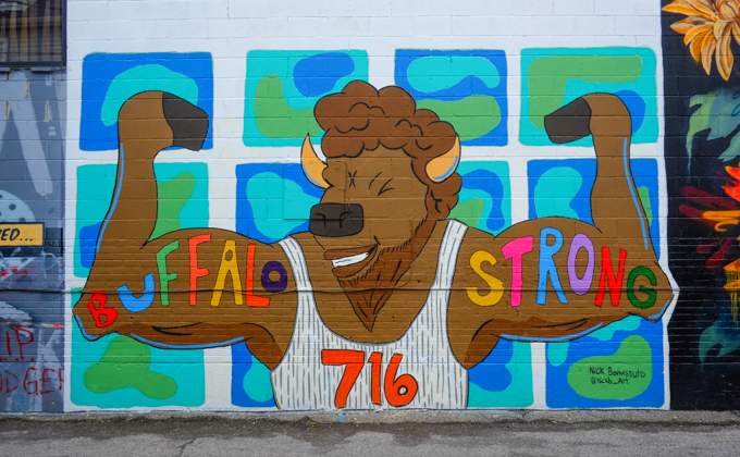 mural in an alley, cartoonish buffalo, standing on hind legs, cheering with front legs as upraised arms, bulging muscles, with the words buffalo strong written on arms