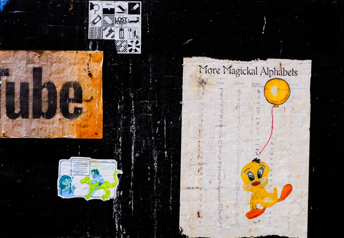 small paper poster graffiti, with tweety bird cartoon character holding a balloon, on the paper is a listing of 3 different alphabets