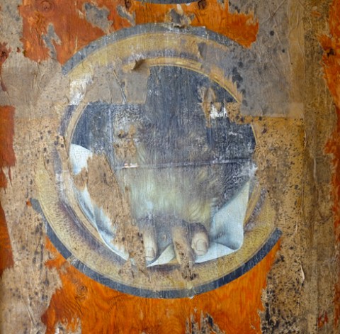 circular paste up that is weathered and torn and hard to see what was once there except for two fingers at the bottom