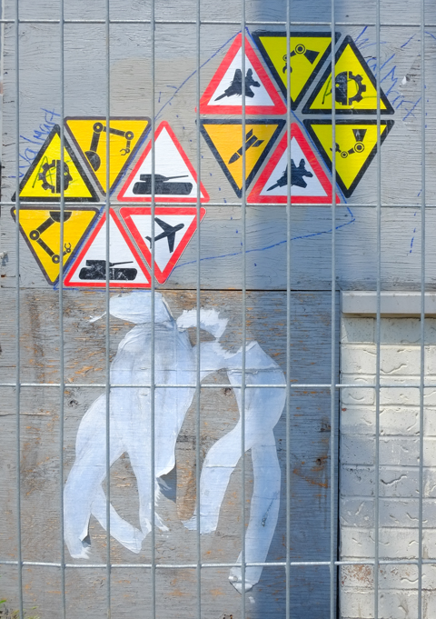 warning signs in triangle shapes, as graffiti paste ups, behind metal construction fence, on building waiting for demolition
