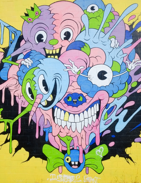 mural by Alex Pardee, on bright yellow background, many weird and ugly monsters and partial faces, a big mouth full of teeth, eyeballs, 
