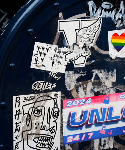 side of a US Postal mailbox with graffiti stickers on it. 