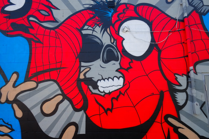 close up of head of character in mural by Matt Gondek in a Wndosr Ontario Alley, large red costume, ripped to show grey skull below, 