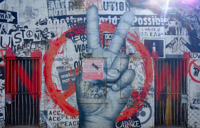 street art painting of a realistic hand, very large, making peace sign with background of protest signs in black and white, as well as a large red spray paint peace symbol
