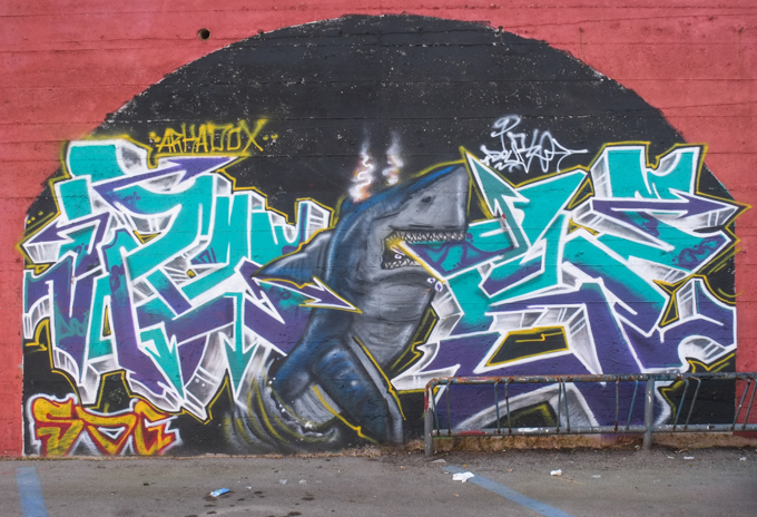 curved wall, exterior, painted, top level in shapes, by Eltono, bottom part in arch shapes with each arch filled in by a different artist, dancing shark