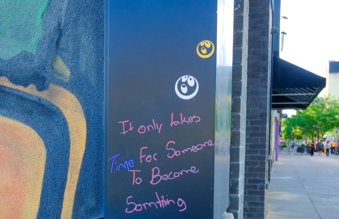 in pink marker, someone has written words on a large mural, text says It only takes time for someone to become something
