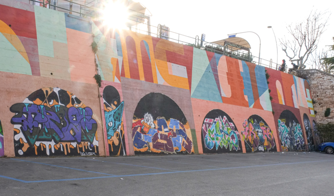 curved wall, exterior, painted, top level in shapes, by Eltono, bottom part in arch shapes with each arch filled in by a different artist