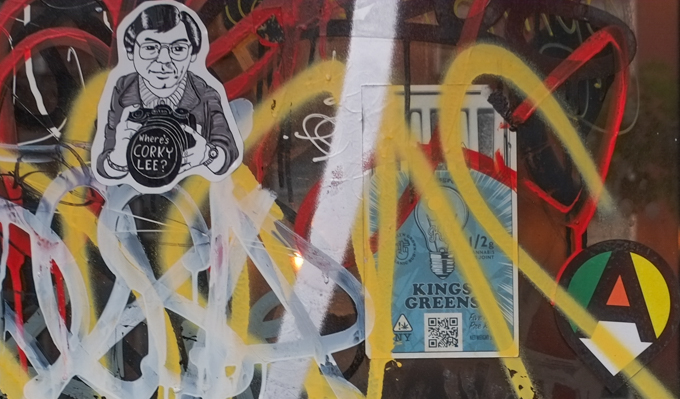 graffiti sticker that says where is corky lee, an asian american photographer who died in 2021, black and white drawing of his portrait, holding a large camera