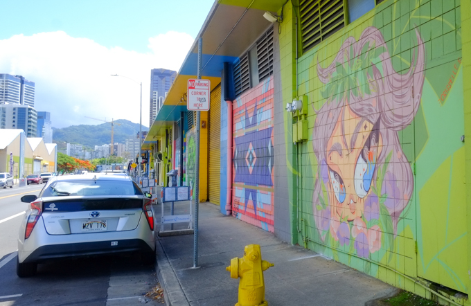 a white car is parked on a street where a building is covered in murals, at the near end is one on bright light green background, a pony's head, 