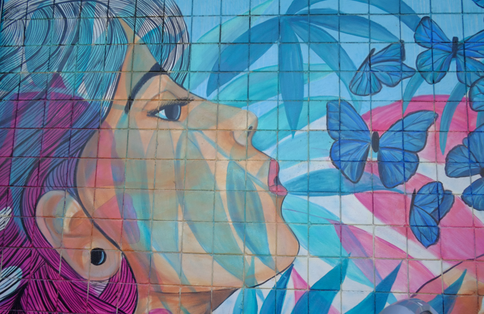 mural by Andrea James, a woman is blowing air towards a small group of blue butterflies