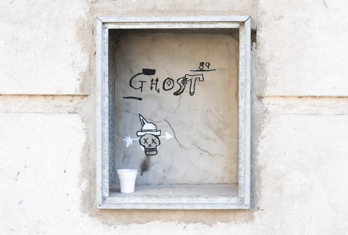 in a niche in a cement wall, wood frame, someone has left behind a white paper up, also the word ghost has been written there along with a little drawing of a skull with a white hat 