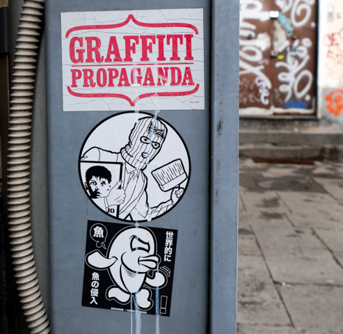 graffiti propaganda, pasteups, mr fish, an image oa person wearing balaclava and carrying a broom and a piece of art to paste on a wall